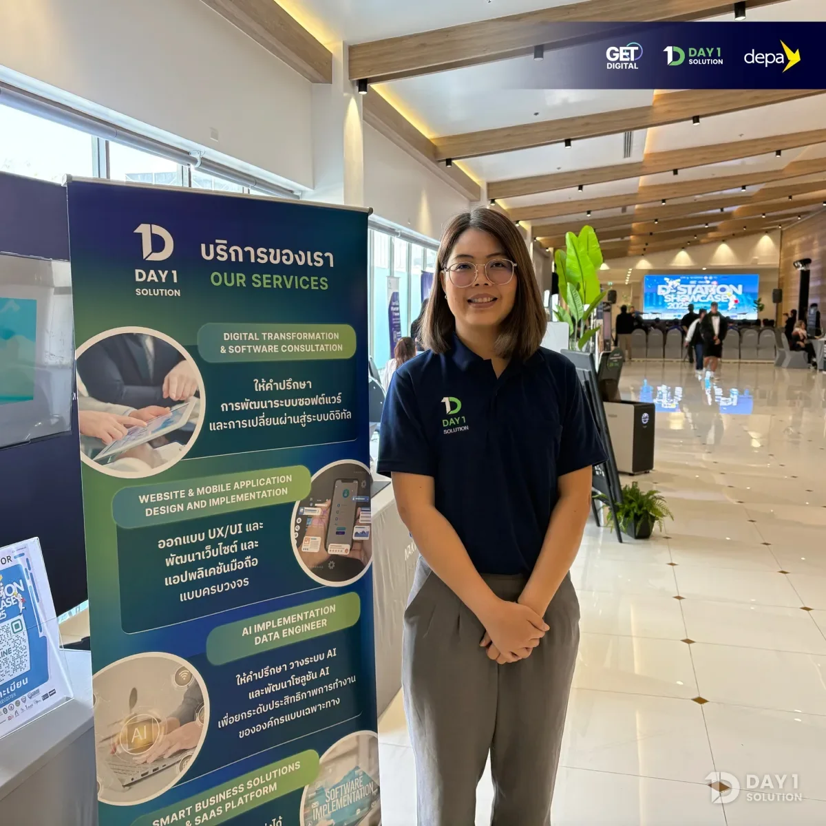 ทีมงาน Day 1 Solution ยืนข้างโรลอัพแสดงบริการของบริษัทที่บูธในงาน D-station Showcase 2025